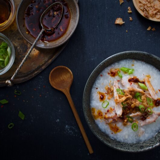 Bubur ajam in een schaaltje, met een lepel en losse ingrediënten