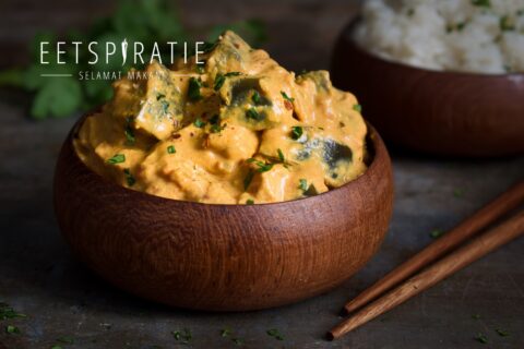 Auberginecurry, stukjes aubergine in een gele curry, geserveerd in een houten bakje met eetstokjes