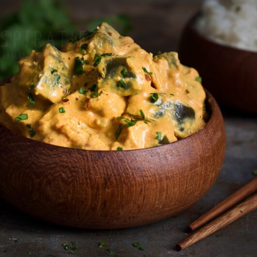 Auberginecurry, stukjes aubergine in een gele curry, geserveerd in een houten bakje met eetstokjes