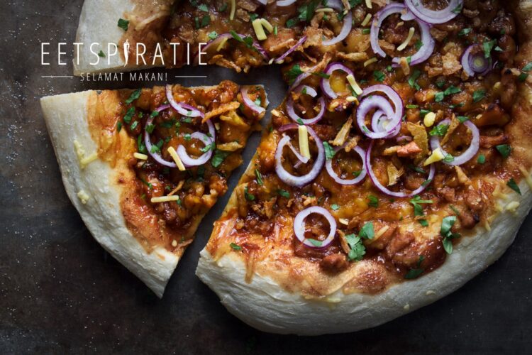 Pizza met barbecuesaus, rode ui, kaas, kipstukjes, koriander en gebakken uitjes. Uit de hele pizza is 1 stuk uitgesneden.