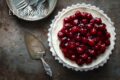 Een vegan MonChou taart met kersentopping van bovenaf gezien met een taartschep en een bordjes met vorkjes ernaast