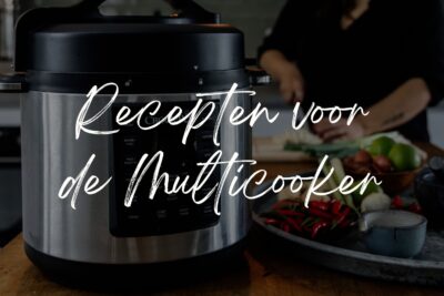 Een multicooker, waarbij iemand op de achtergrond groenten aan het snijden is. Tekst op de foto: recepten voor de multicooker