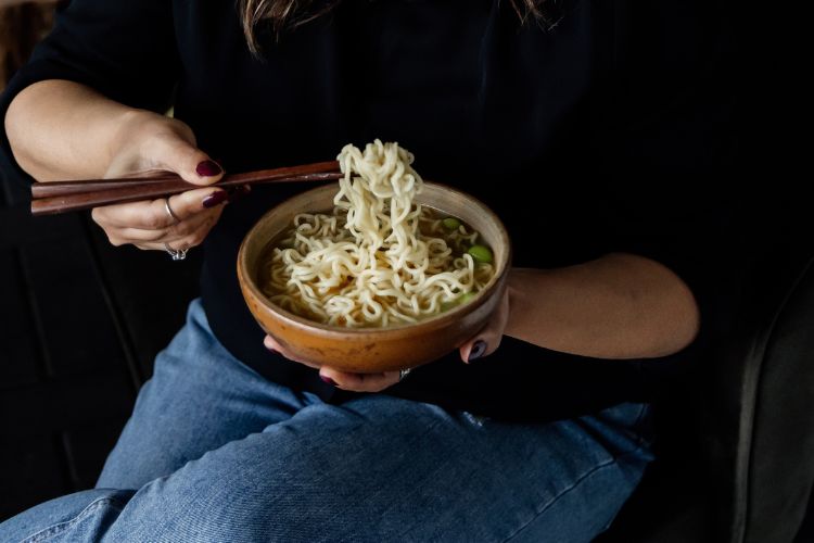 Een kommetje noedels met stokjes eten